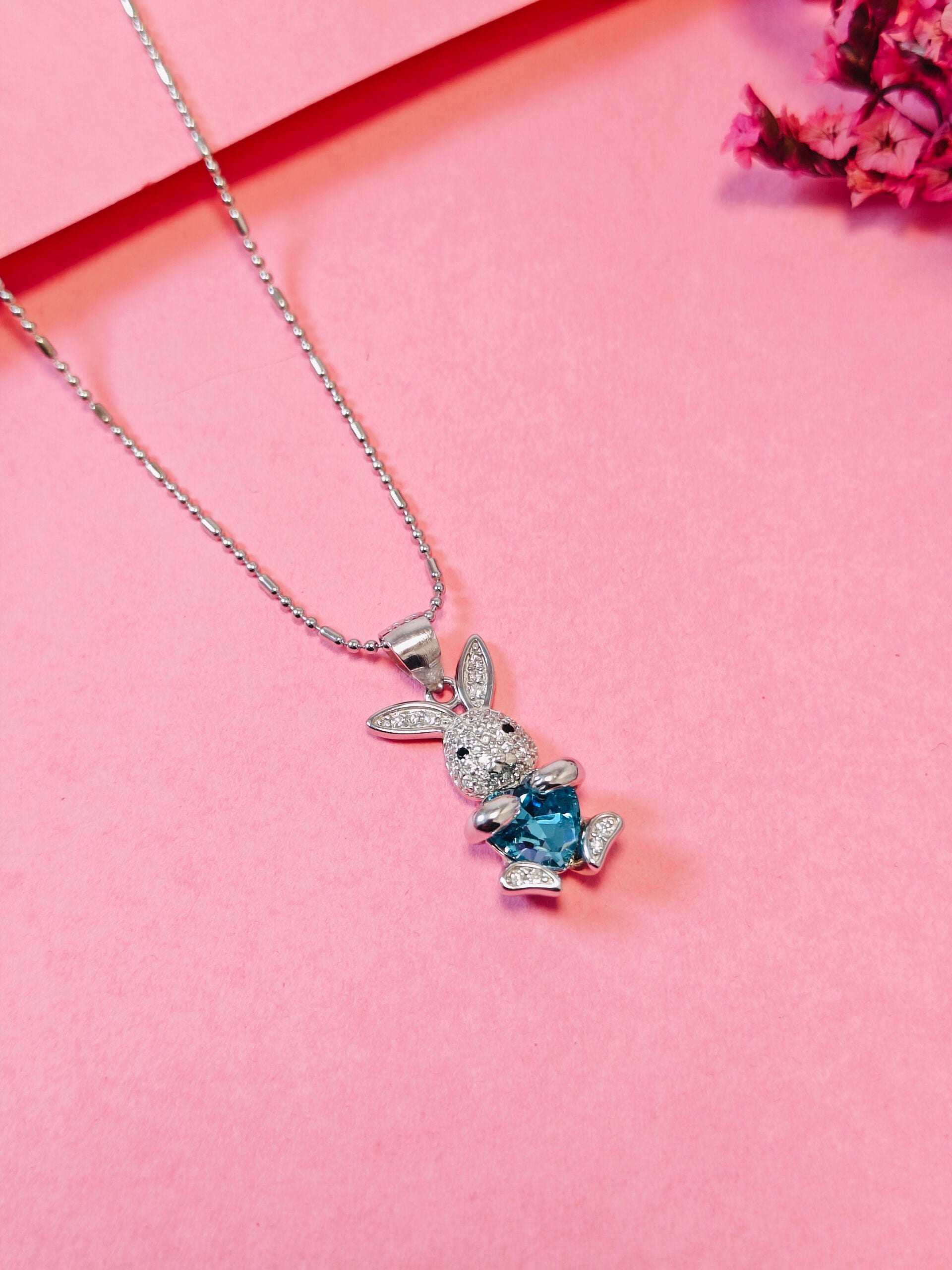 Silver bunny pendant with a blue gemstone on a pink background